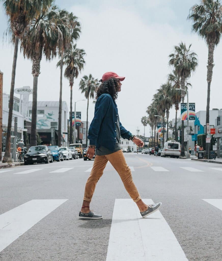 A woman walking across a crosswalk in a sunny urban area with palm trees and shops.