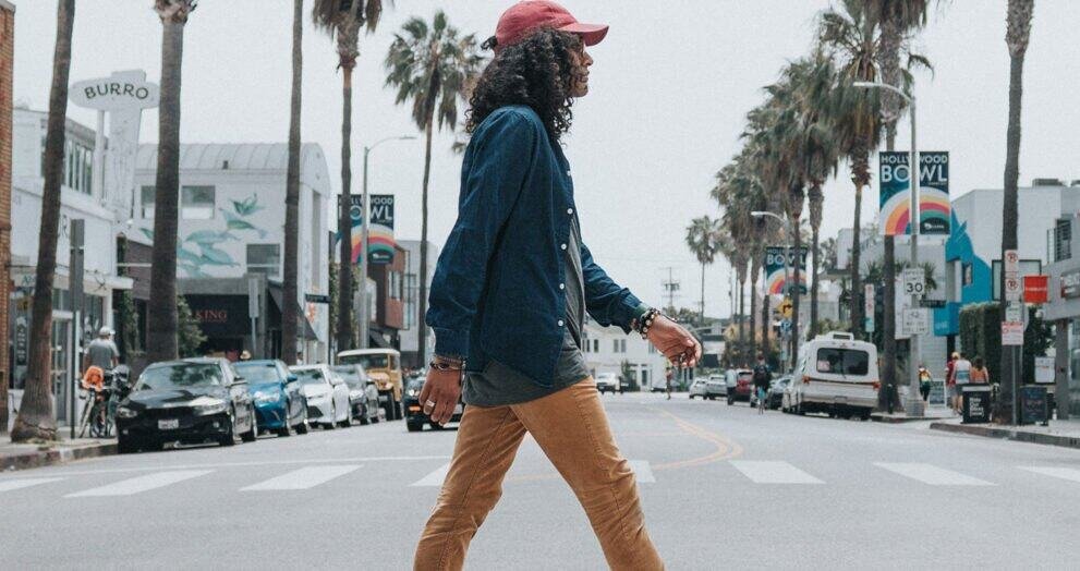 A woman walking across a crosswalk in a sunny urban area with palm trees and shops.