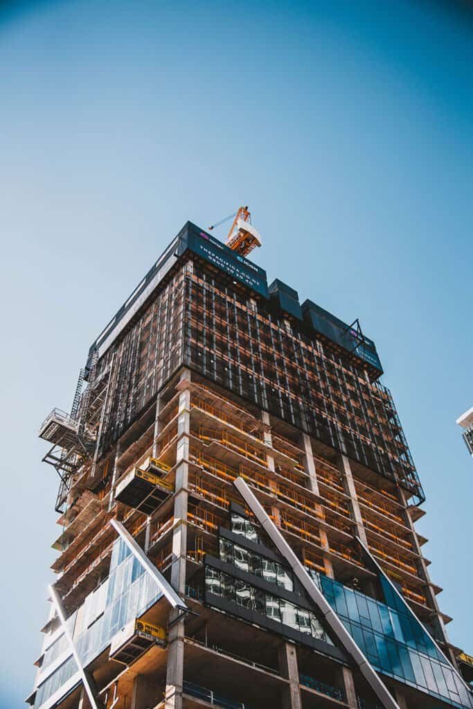 Modern skyscraper under construction with scaffolding and cranes against blue sky.