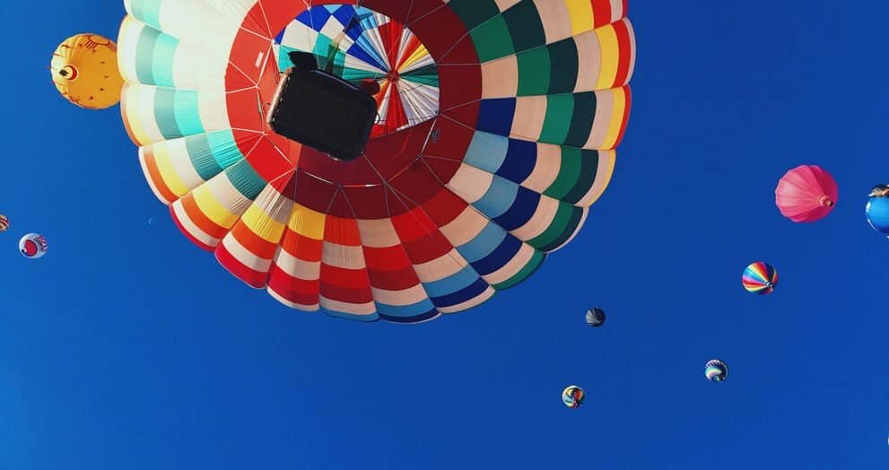 Colorful hot air balloons flying in a clear blue sky, with a focus on one balloon’s vibrant pattern.