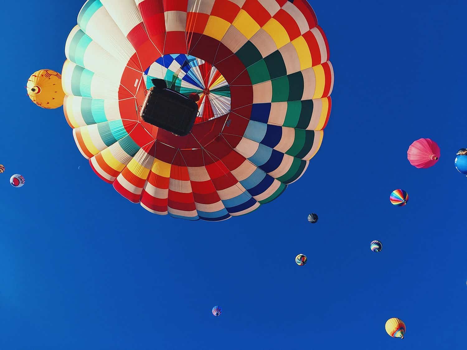 Colorful hot air balloons flying in a clear blue sky, with a focus on one balloon’s vibrant pattern.